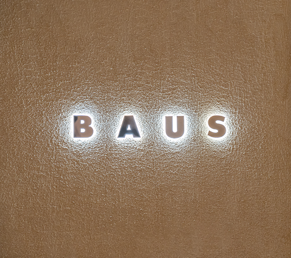 質感のある壁に照明で浮かび上がるBAUSの文字看板