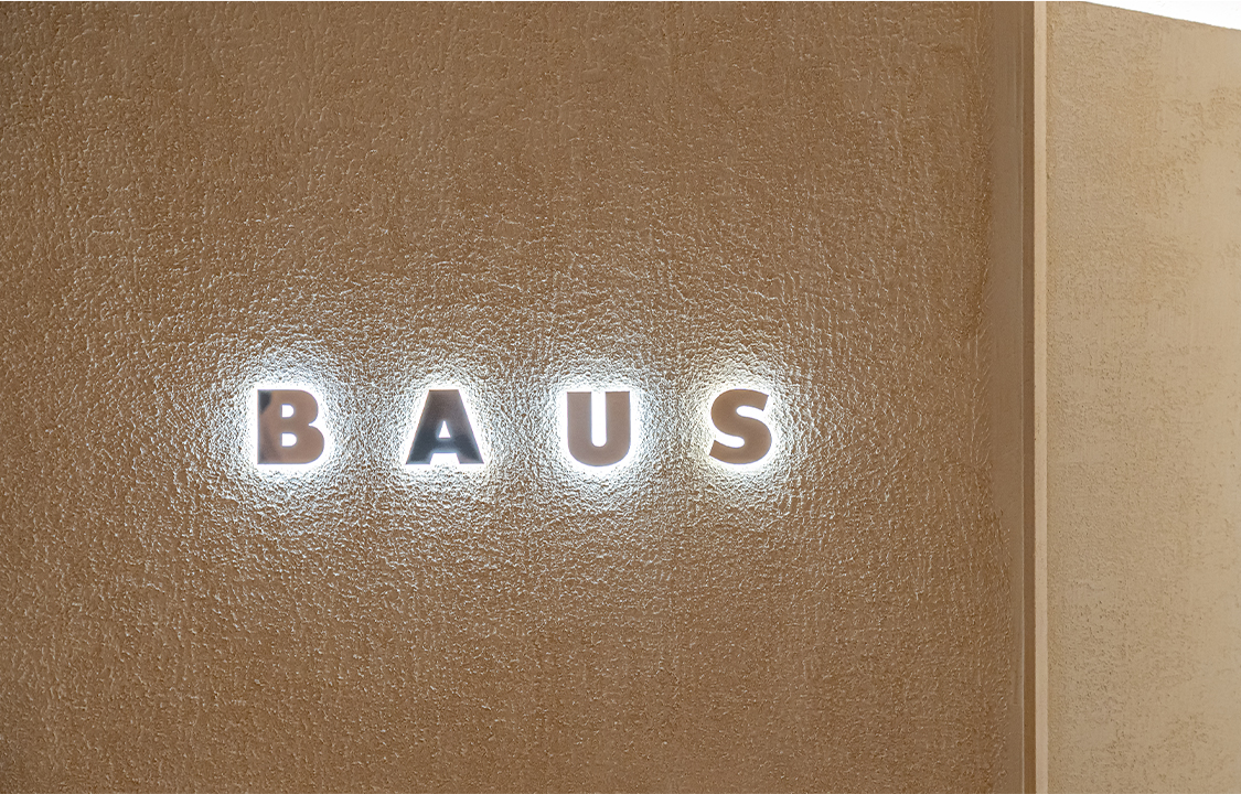 質感のある壁に照明で浮かび上がるBAUSの文字看板