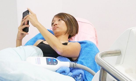 クールスカルプティング施術中に横になってスマートフォンを見る女性